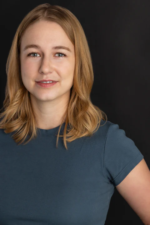 Katie Peabody headshot — slate-blue tee, charcoal background, warm smile