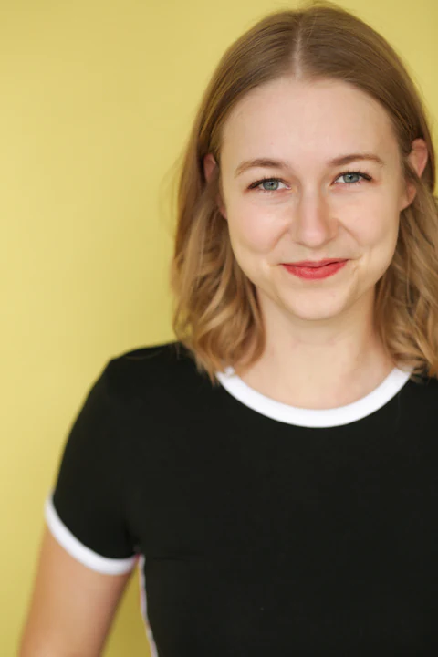 Katie Peabody headshot — black crew-neck tee, yellow background, smiling