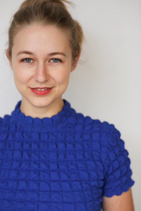 Katie Peabody headshot — cobalt textured knit top, hair up, pale background