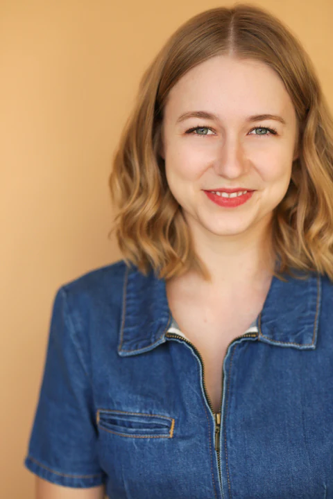 Katie Peabody headshot — denim zip jumpsuit, warm apricot background