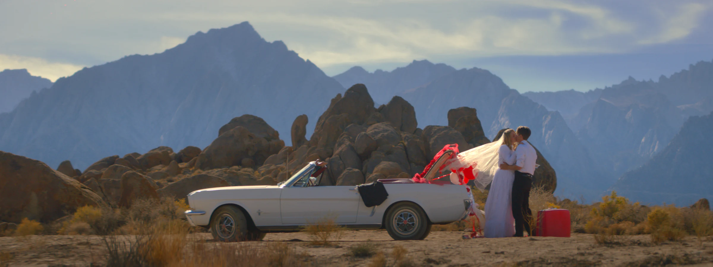 A convertible parked in the desert with a figure in white beside it, from the short film Anniversary