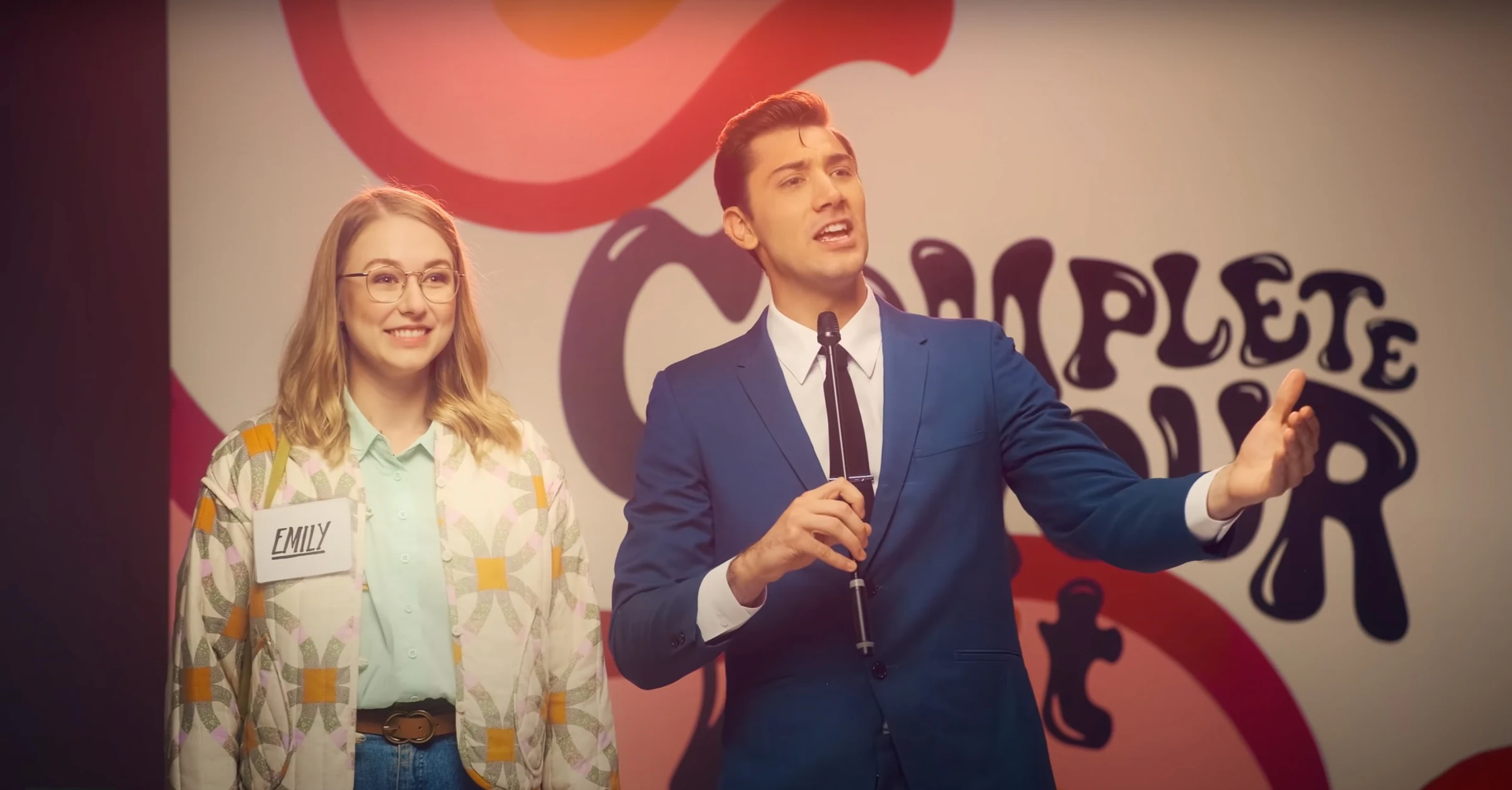 Katie Peabody with a presenter in front of a brightly patterned backdrop, from a Fujifilm commercial