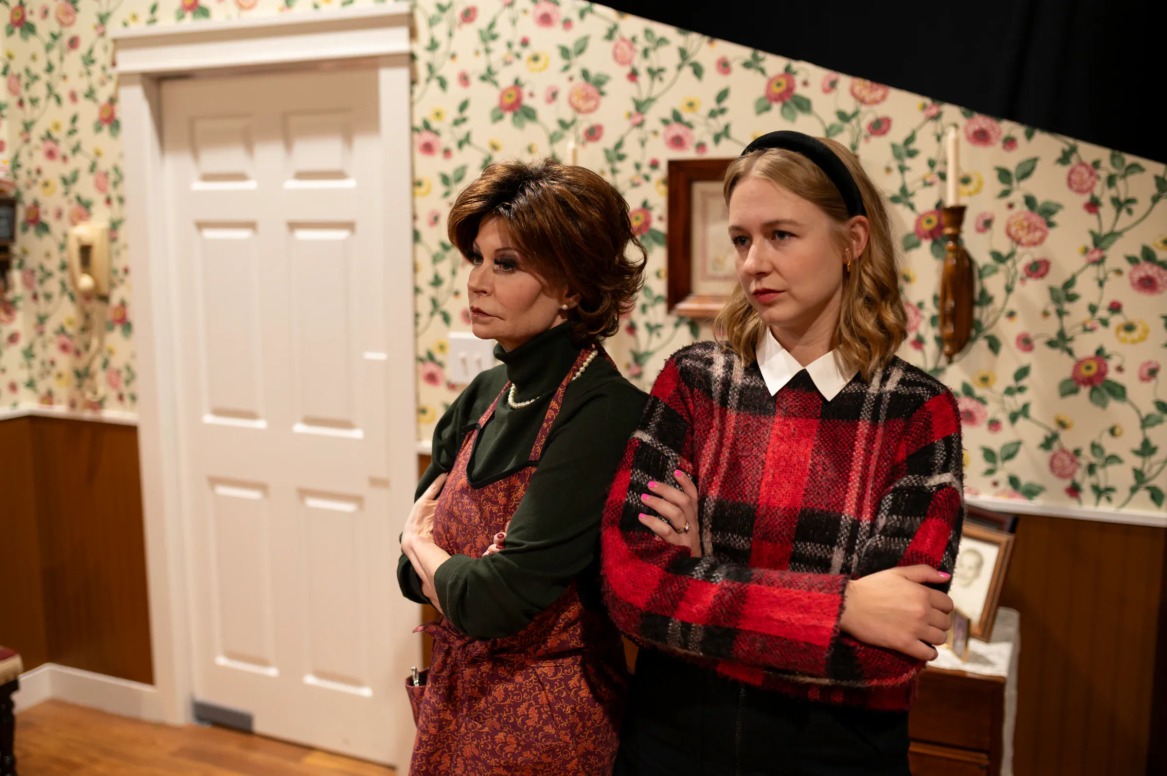 Katie Peabody as Leslie facing another character against floral wallpaper in Feast of Fools, Harvest Theater Company