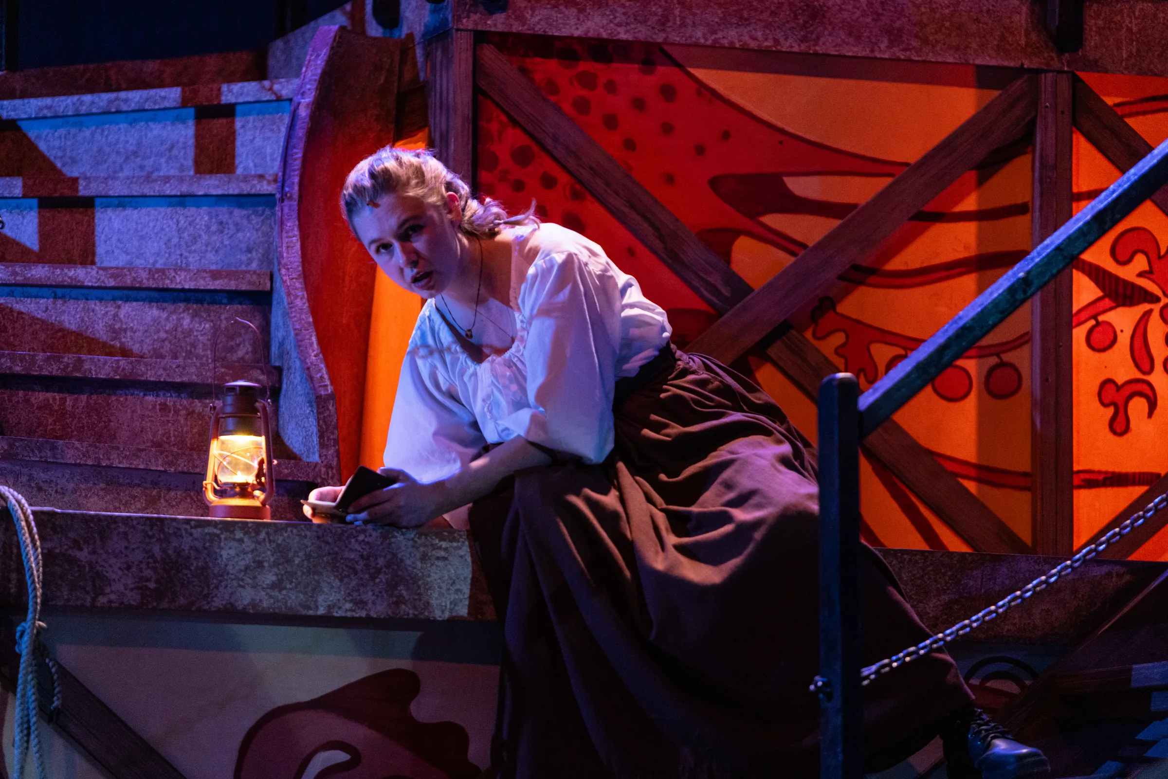Katie Peabody as Abigail Burgess in Matinicus: A Lighthouse Play, seated with a lit lantern beside the painted set