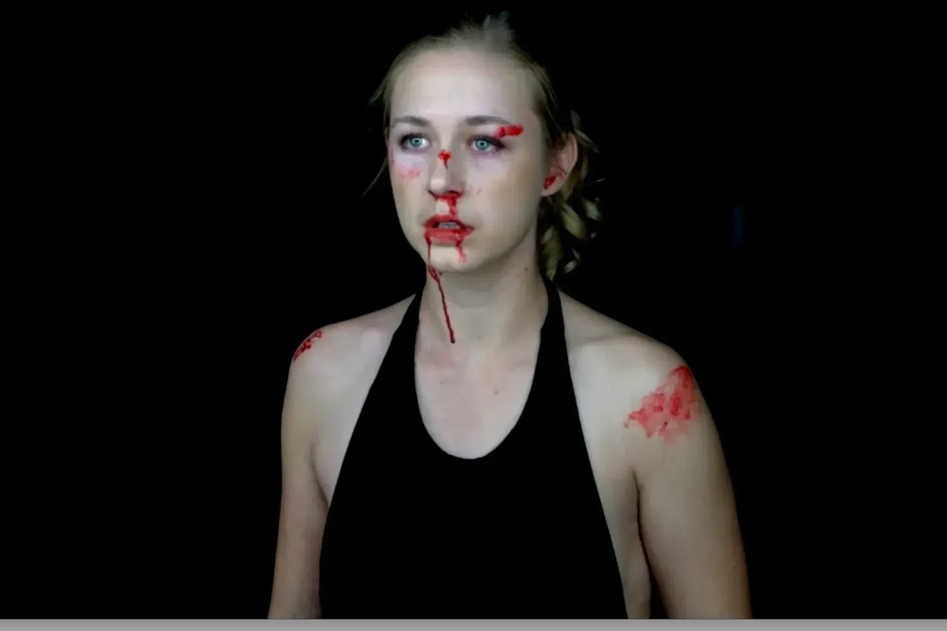 Katie Peabody with stage blood on her face and shoulder against black, from the short film When It's Warmer Outside